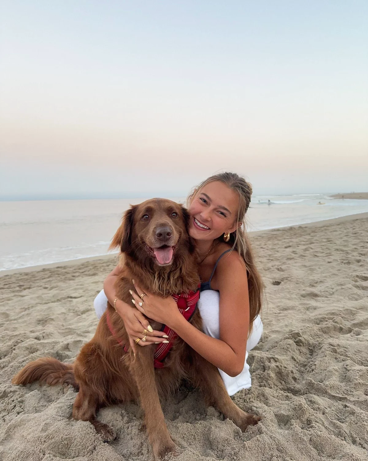 Propriétaire heureuse serrant son chien dans les bras sur la plage au coucher du soleil